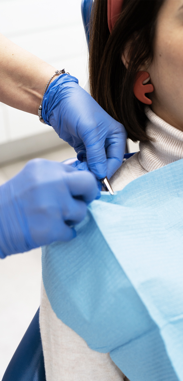 "A close-up of a dentist's gloved hands holding dental instruments, preparing for a procedure on a patient covered with a protective bib.