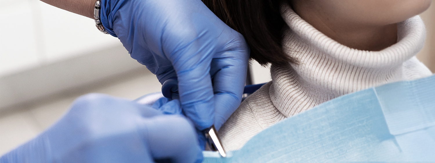 A close-up of a dentist's gloved hands holding dental instruments, preparing for a procedure on a patient covered with a protective bib. mobile